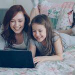 Mother and daughter laugh while using a laptop.