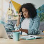 Young woman talking on phone at laptop desk.