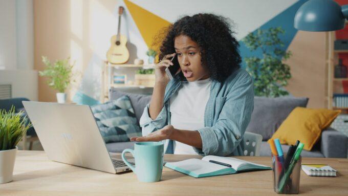 Young woman talking on phone at laptop desk.