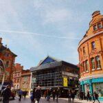 people walking beside buildings under cloudy sky with contrail